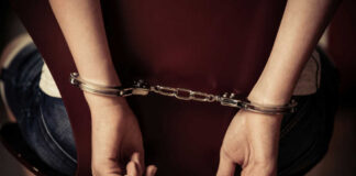 Hands handcuffed behind a chair, viewed from the back