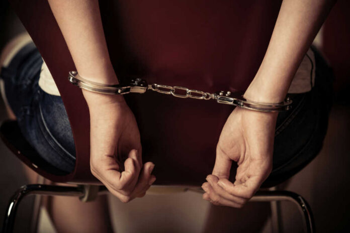 shutterstock577235971jpg-1 Hands handcuffed behind a chair, viewed from the back
