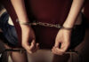 Hands handcuffed behind a chair, viewed from the back
