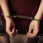 Hands handcuffed behind a chair, viewed from the back