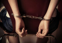 Hands handcuffed behind a chair, viewed from the back