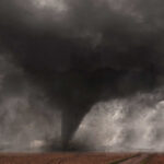 A tornado forming in a dark, stormy sky over a field