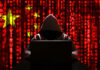 Espionage Blitz Targets U.S. AI A hooded figure sitting in front of a laptop with a red digital background