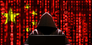 A hooded figure sitting in front of a laptop with a red digital background