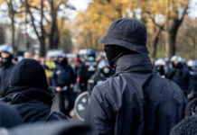 Daylight Abduction Try—Suspect Still Loose A crowd of masked individuals facing law enforcement in an autumn setting