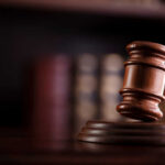 Congressman’s Gambles Rattle DOJ A wooden gavel resting on a sound block with blurred law books in the background