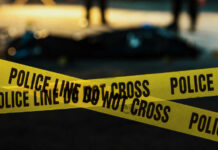 Yellow police caution tape at a crime scene with blurred figures in the background
