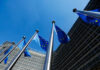 Cocaine Fugitive Triggers EU Aid Showdown European Union flags flying in front of a modern building against a clear blue sky
