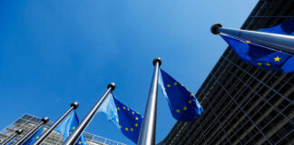European Union flags flying in front of a modern building against a clear blue sky