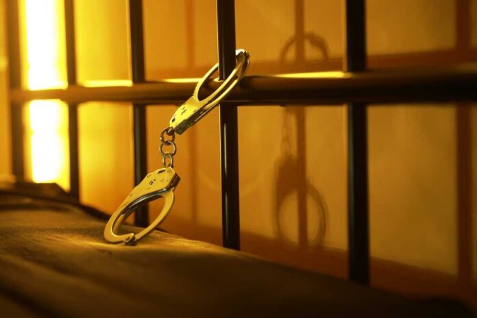 Handcuffs,Against,Jail,Cell,Bars,With,Warm,Lighting,-,Concept Close-up of handcuffs attached to a bed frame