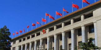 Facade of a government building adorned with red flags and a national emblem