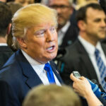 A man speaking to reporters at a press event surrounded by media personnel