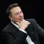 Elon Revives GOP Turnout Machine Man in suit smiling, resting chin on hand.
