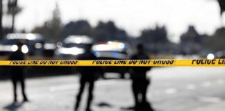 Police tape cordons off a street with blurred officers and vehicles in the background