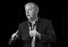 Man in a suit speaking into a handheld microphone
