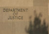 Citizenship Revocations Hit Modern Highs Sign reading Department of Justice on a stone wall with a shadow
