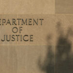 Sign reading Department of Justice on a stone wall with a shadow