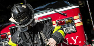 Firefighter adjusting gear in front of a fire truck