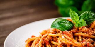 Spaghetti bolognese topped with basil on a white plate