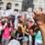 Clerk Stops Ex-SEAL’s Explosive Protest Plot Raised fist in foreground at a crowded street protest
