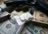 Pills in a plastic bag on stacks of U.S. dollars with a handgun nearby
