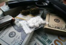 Pills in a plastic bag on stacks of U.S. dollars with a handgun nearby