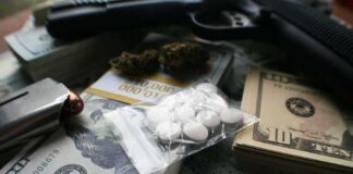 Pills in a plastic bag on stacks of U.S. dollars with a handgun nearby