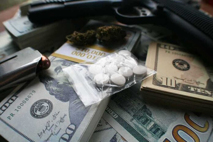 shutterstock_1325340281 Pills in a plastic bag on stacks of U.S. dollars with a handgun nearby