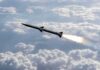 Iran Launches New Strikes On U.S. Bases Rocket flying above clouds with bright exhaust plume