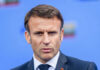 Close-up portrait of a serious-looking male political leader in formal attire against a blue background