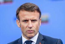 Close-up portrait of a serious-looking male political leader in formal attire against a blue background