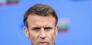 Close-up portrait of a serious-looking male political leader in formal attire against a blue background