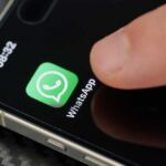 Finger tapping the WhatsApp icon on a smartphone screen