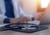 Berlin Doctor Convicted Of Fifteen Murders A stethoscope resting on a tablet with a blurred medical professional in the background typing on a laptop