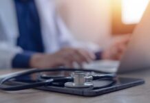 Berlin Doctor Convicted Of Fifteen Murders A stethoscope resting on a tablet with a blurred medical professional in the background typing on a laptop