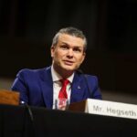 Hegseth Reverses Apache Pilot Suspensions Man in a blue suit speaking at a government hearing