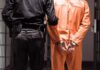 Prisoner in orange jumpsuit handcuffed with guard standing beside