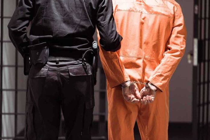 Prisoner in orange jumpsuit handcuffed with guard standing beside