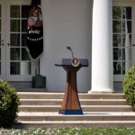 DA Vows To Blow Up Trump’s Ballroom Podium with presidential seal in a garden colonnade