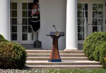 DA Vows To Blow Up Trump’s Ballroom Podium with presidential seal in a garden colonnade