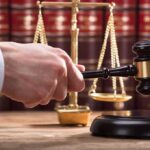 Judge's hand holding gavel near scales of justice
