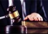 Judge's gavel striking block with hand on book in background