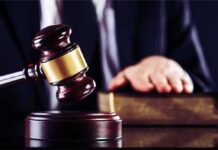 Judge's gavel striking block with hand on book in background