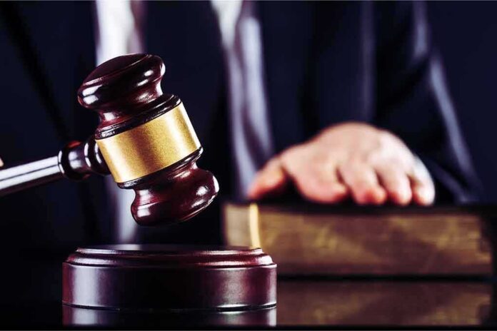 shutterstock_1182666757 Judge's gavel striking block with hand on book in background