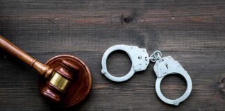 Judge's gavel and metal handcuffs on wooden table