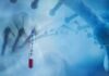 Fauci Texts Put Vaccine Messaging Under Scrutiny Gloved hand holding a COVID-19 test tube beside a stylized DNA helix