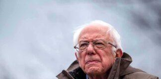 elderly man in glasses speaking outdoors into microphones