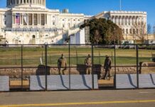 Soldiers stand behind a security fence near a large government building