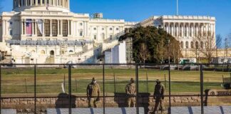 Soldiers stand behind a security fence near a large government building