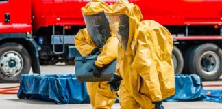 Hazmat workers in yellow suits carry equipment near a tanker truck